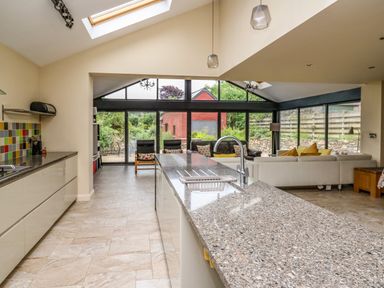 A kitchen and living area with a granite island sink sofa and glass sliding doors at Nevern House in Newport Pembrokeshire