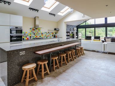 A kitchen with a long island and wooden stools next to a living area with sofas and large windows at Nevern House in Newport Pembrokeshire