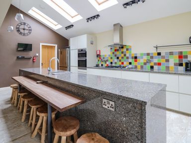 A kitchen with a large island and wooden stools under a wooden counter at Nevern House in Newport Pembrokeshire