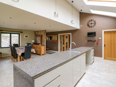 A kitchen with a long island and sink a dining table with chairs and a clock on the wall at Nevern House in Newport Pembrokeshire