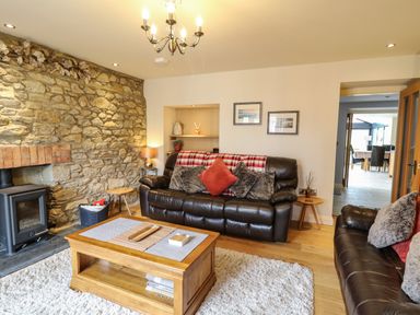 A living room with leather sofas a stone wall fireplace wooden coffee table and a chandelier at Nevern House Newport Pembrokeshire