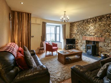 A living room with leather sofas a wooden coffee table a stone wall fireplace and a red armchair at Nevern House Newport Pembrokeshire