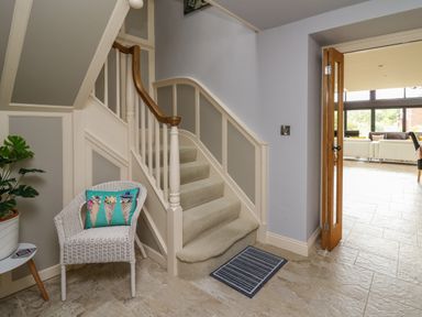 A staircase with beige carpet and wooden handrail next to a white wicker chair with a colorful cushion in a hallway at Nevern House in Newport Pembrokeshire
