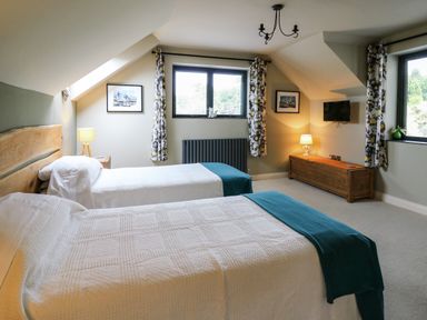 A bedroom with two single beds a wooden chest and windows with floral curtains at Nevern House in Newport Pembrokeshire