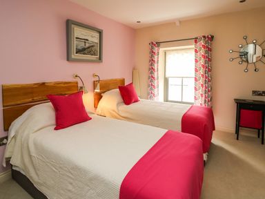 A bedroom with two single beds with red pillows and blankets by a window with patterned curtains at Nevern House in Newport Pembrokeshire