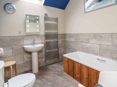 A bathroom with a white pedestal sink a toilet a bathtub with wooden paneling a stool a wall-mounted towel radiator and a clock at Nevern House Newport Pembrokeshire