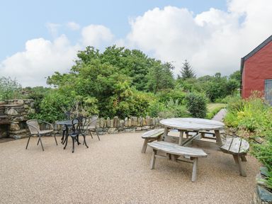 An outdoor patio with a wooden round picnic table and a small black metal table with four chairs at Nevern House in Newport Pembrokeshire