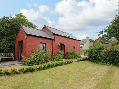 A red house with a slate roof and garden with green shrubs and lawn at Nevern House in Newport Pembrokeshire