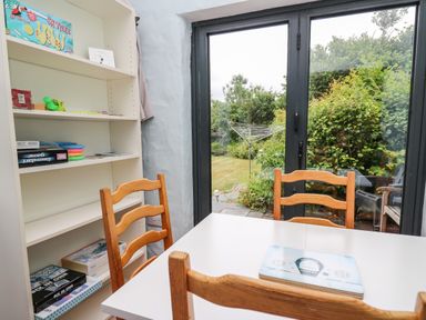 A dining area with a white table and wooden chairs next to a white bookshelf and glass doors opening to a garden at Nevern House in Newport Pembrokeshire