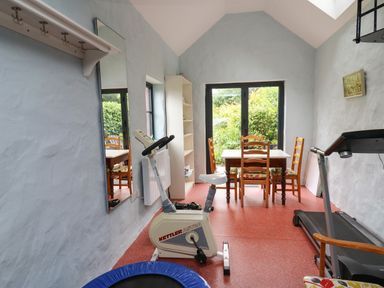 A room with exercise equipment a table with four chairs a mirror and a bookshelf at Nevern House in Newport Pembrokeshire
