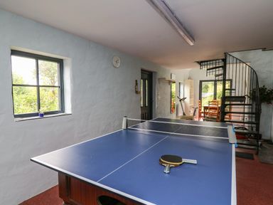 A room with a blue table tennis table and paddles a spiral staircase and wooden dining table with chairs at Nevern House in Newport Pembrokeshire