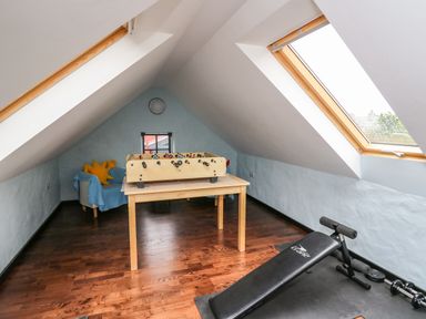 An attic room with foosball table on a wooden table a blue chair with pillows and exercise bench near skylight windows at Nevern House in Newport Pembrokeshire