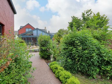A garden pathway with shrubs and bushes leading to a house with a glass extension at Nevern House in Newport Pembrokeshire
