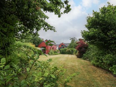 A garden with a lawn surrounded by bushes and trees with red houses in the background at Nevern House in Newport Pembrokeshire