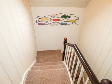 A carpeted staircase with white walls and a wooden handrail with a fish decoration on the wall at Panteg Cottage Newport