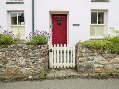 A front entrance with a red door white picket gate and stone walls with plants at Panteg Cottage Newport Pembrokeshire