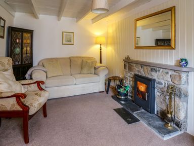 A living room with a beige sofa a floral armchair a stone fireplace and a floor lamp at Panteg Cottage Newport