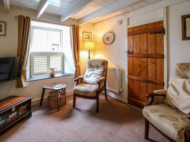 A sitting room with two upholstered armchairs a wooden side table with a wicker basket a window with shutters and curtains a wooden door and a floor lamp at Panteg Cottage Newport