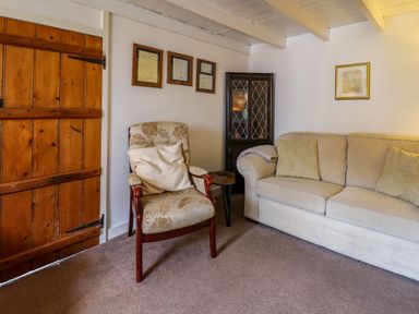 A living room with a wooden door an armchair a beige sofa and framed pictures on the wall at Panteg Cottage Newport