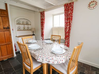 A dining room with a round table set for four near a window with red curtains at Panteg Cottage Newport