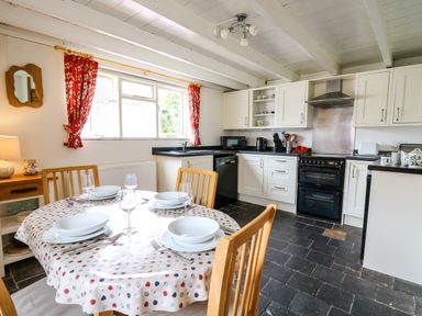 A kitchen with a dining table set with plates and glasses and wooden chairs at Panteg Cottage Newport Pembrokeshire