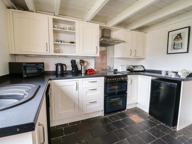 A kitchen with white cabinets black countertops a black oven a black microwave a black kettle a black mini fridge and a framed picture on the wall at Panteg Cottage Newport
