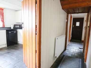 A hallway with a wooden door open to a kitchen with black appliances and white cabinets at Panteg Cottage Newport