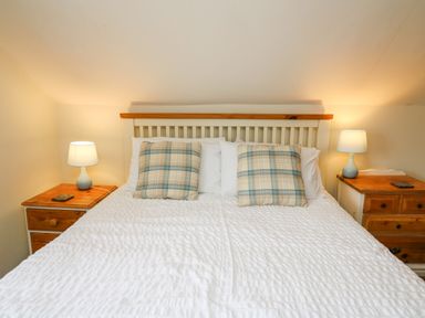 A bedroom with a white bedspread two plaid pillows a wooden headboard wooden nightstands and lamps at Panteg Cottage Newport