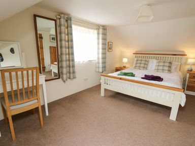 A bedroom with a double bed with plaid pillows and folded towels bedside tables with lamps a wooden chair and white dressing table in Panteg Cottage Newport