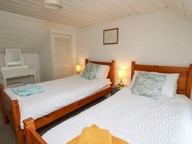 A bedroom with two single wooden beds with white bedspreads and decorative pillows a nightstand with a lamp a dressing table with a mirror and a small closet at Panteg Cottage Newport