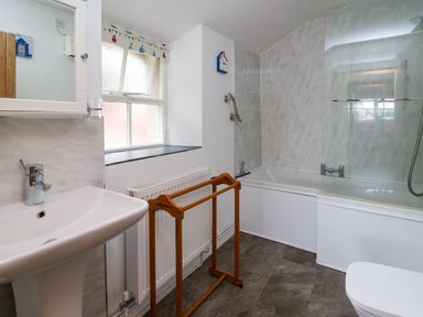 A bathroom with a sink radiator wooden towel rack bathtub with glass screen and window at Panteg Cottage Newport