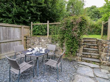 An outdoor patio area with a table set for tea and four chairs surrounded by stone walls and steps at Panteg Cottage Newport