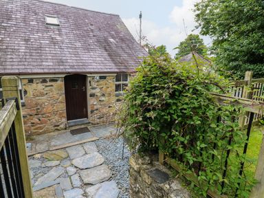 An exterior view of a stone cottage with a wooden door a stone pathway and green plants on a fence at Panteg Cottage Newport Pembrokeshire