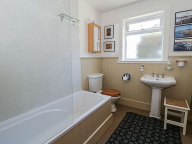 A bathroom with a bathtub, toilet, sink, and wall pictures at Dolwylan Newport, Pembrokeshire