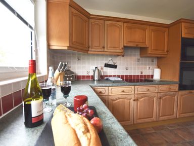 A kitchen with wooden cabinets green countertop wine bottle glasses bread fruit and kettle at Greenfields in St Davids Pembrokeshire