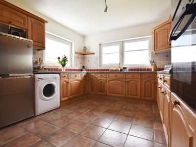 A kitchen with wooden cabinets a washing machine a refrigerator flowers on the counter and tile flooring at Greenfields in St Davids Pembrokeshire