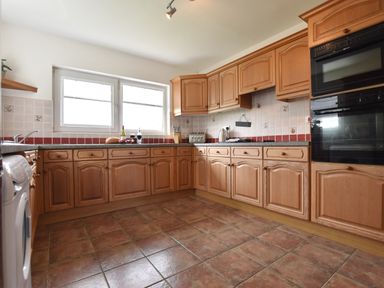 A kitchen with wooden cabinets tiled floor and countertop with a window above at Greenfields in St Davids Pembrokeshire