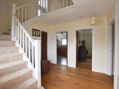 A hallway with carpeted stairs wooden floor and doors leading to a kitchen and living room at Greenfields in St Davids Pembrokeshire