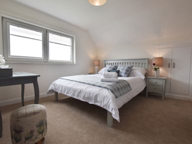 A bedroom with a bed pillows bedside tables lamps a desk and a small upholstered stool at Greenfields in St Davids Pembrokeshire