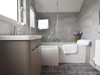 A bathroom with a sink cabinet a bathtub with a glass shower screen white towels and flowers at Greenfields in St Davids Pembrokeshire