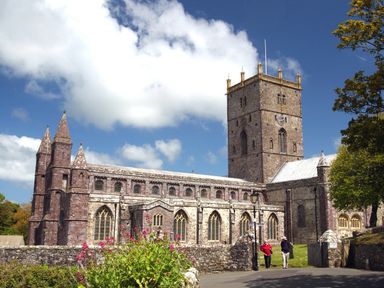 A large historic stone cathedral with a tall square tower and pointed arches with two people walking near the entrance at Greenfields in St Davids Pembrokeshire