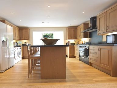 A kitchen with wooden cabinets a kitchen island with chairs a refrigerator and a stove at Gwelfor Newport in Newport Pembrokeshire
