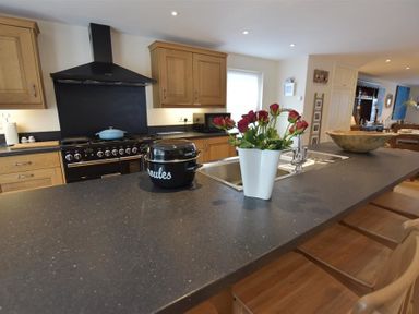 A kitchen with wooden cabinets a black stove a countertop with a sink flowers in a vase and wooden stools at Gwelfor Newport in Newport Pembrokeshire