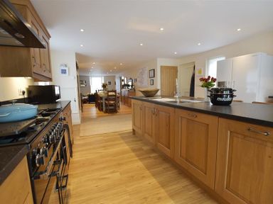 A kitchen with wooden cabinets a black countertop a stove and a sink with a dining area in the background at Gwelfor Newport in Newport Pembrokeshire