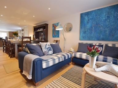A living room with blue and white sofas a round wooden table with flowers and a dining area with wooden chairs in the background at Gwelfor Newport in Newport Pembrokeshire