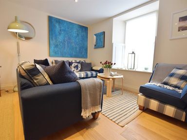 A living room with two blue sofas a round wooden coffee table and a window with a white curtain at Gwelfor Newport in Newport Pembrokeshire