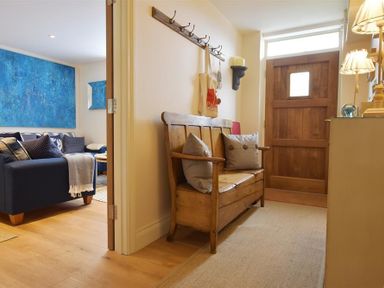 A hallway with a wooden bench and cushions near a wooden door next to a room with a navy sofa and blue wall art at Gwelfor Newport in Newport Pembrokeshire