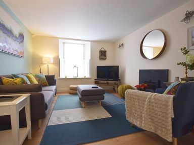 A living room with a grey sofa and armchair a round mirror and a television at Gwelfor Newport in Newport Pembrokeshire