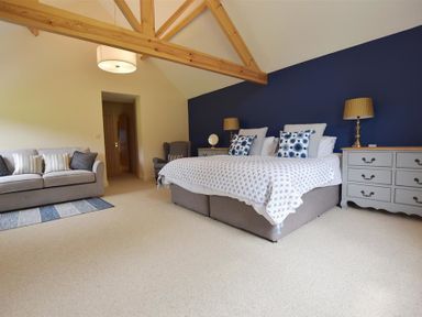 A bedroom with a bed sofa armchair bedside tables and wooden ceiling beams at Gwelfor Newport