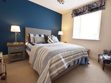 A bedroom with a bed against a blue wall two bedside tables with lamps and a window with patterned curtains at Gwelfor Newport in Newport Pembrokeshire